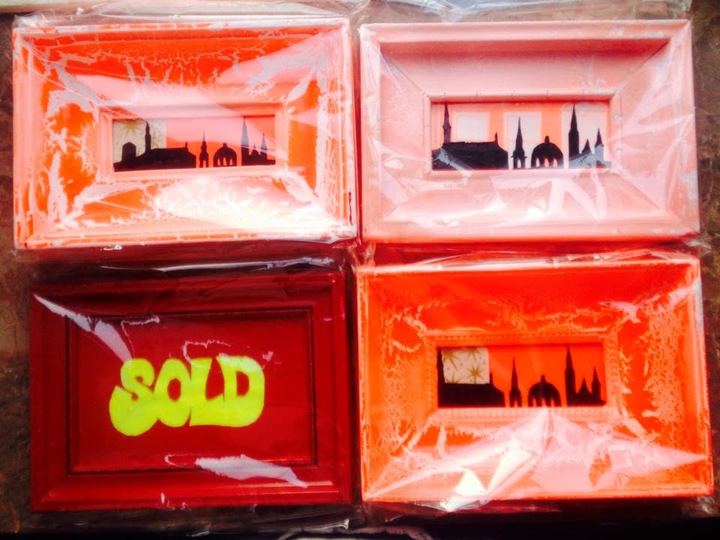 Fire små værker i orange og røde rammer med Københavns tårne som sort silhuet; på én sidder et gult SOLD-mærke.