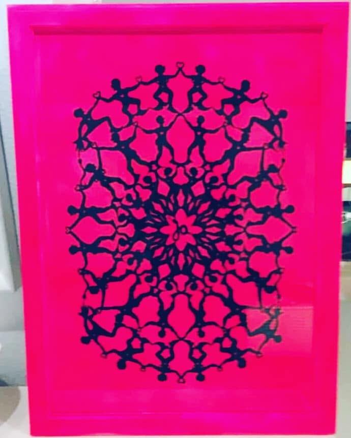 Mørkeblåt, rundt papirklip af små mennesker i kreds, monteret på pink i en pink ramme.