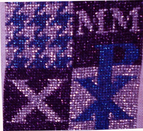 Broderi i lilla og blå metaltråd delt i felter med stjerner, bogstaver, et kryds og et Kristusmonogram.