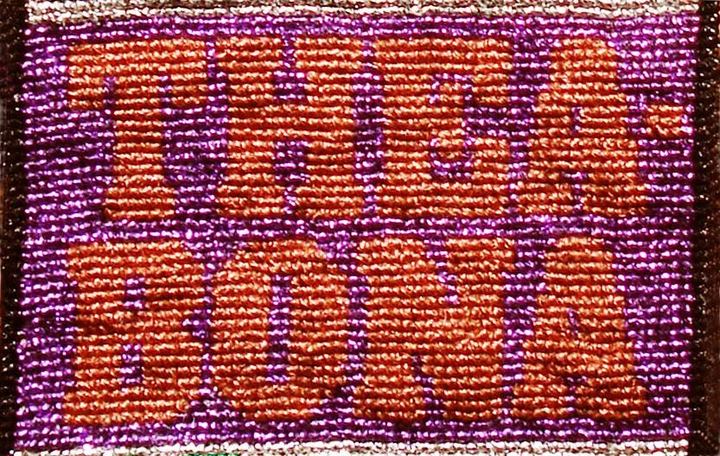 Broderi i lilla og orange metaltråd med bogstaverne THEA BONA.