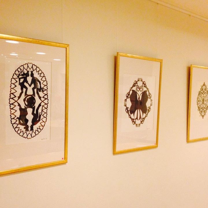 Tre store papirklip i guldrammer hænger på række på en gullig væg.